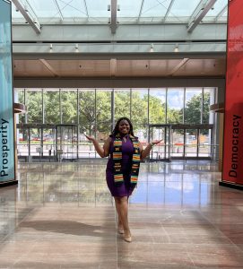 Jaszwan Veal poses for a photo wearing a scarf and standing in front of glass windows inside a campus building at Howard University