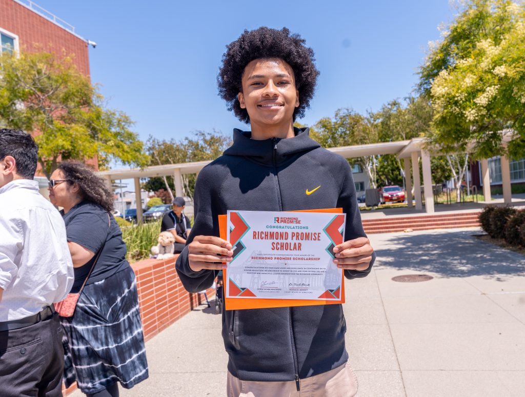 A student wearing a black sweatshirt poses with his RP Scholar Certificate during the RP Scholar Celebration on August 3, 2024.