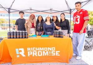 Richmond Promise student staff pose for a photo behind a table with an orange Richmond Promise tablecloth at the 2024 RP Scholar Celebration.