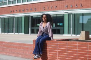 Chandani Battle poses for a photo while sitting on a brick ledge in front of Richmond City Hall