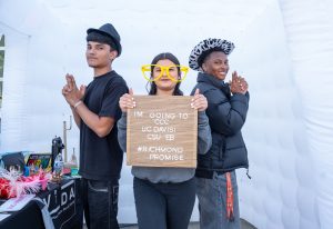 Three new Richmond Promise Scholars pose for a photo with a sign that says "