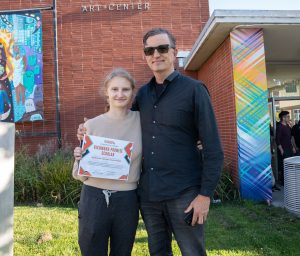 A new Richmond Promise Scholar poses for a photo holding their Richmond Promise Scholarship certificate outside the 2025 Scholar Celebration